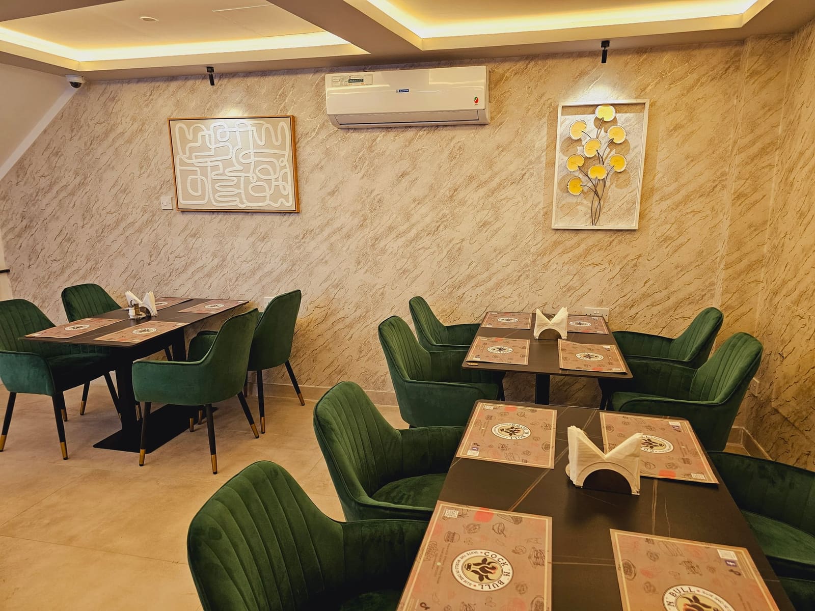 ركن طعام دافئ في الطابق السفلي بمطعم كوك أن بول الشارقة بكراسي مخملية خضراء ولوحات فنية مؤطرة