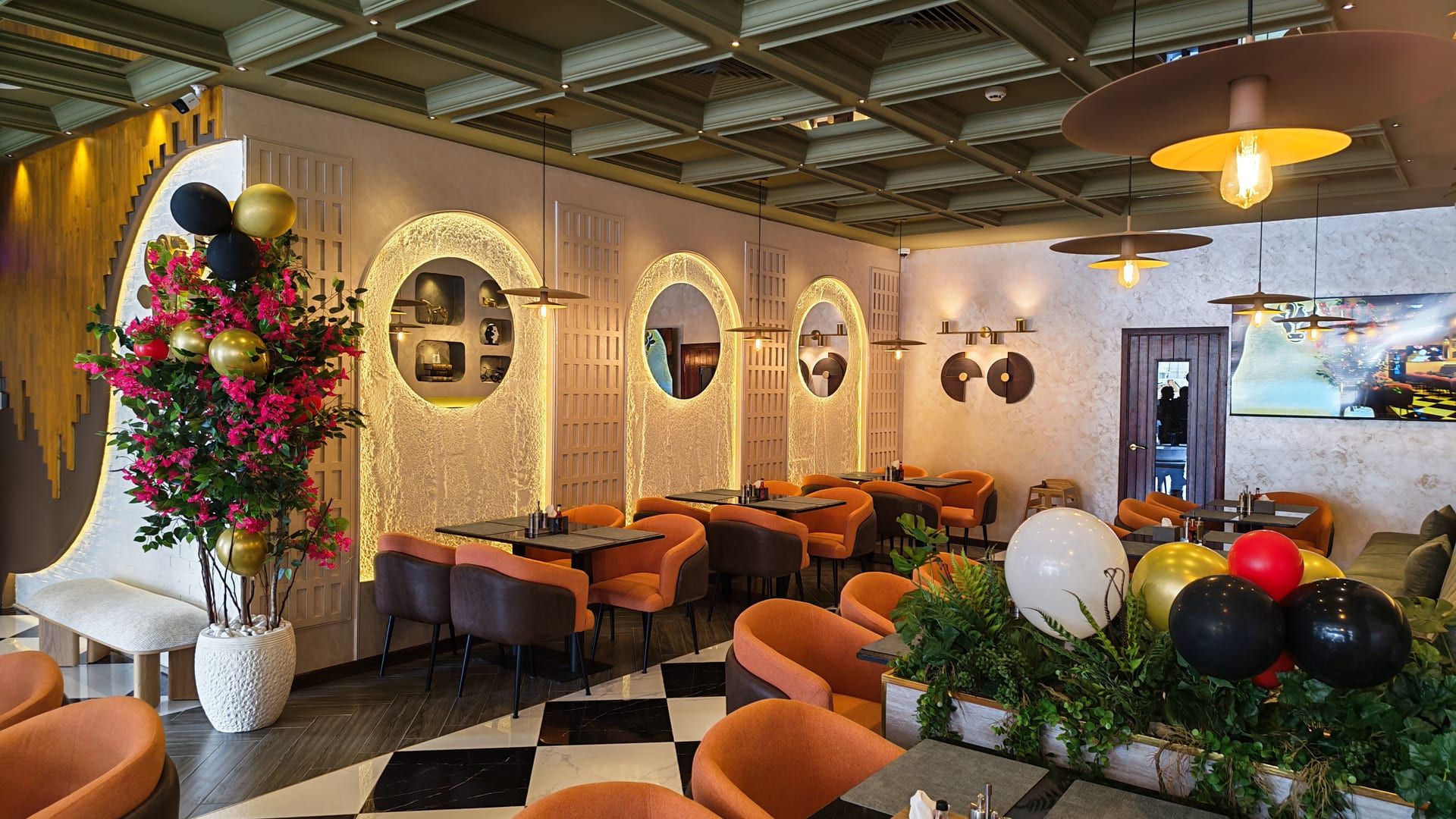 Dining room inside Cock "N" Bull Dubai: green coffered ceiling, checkered marble floor, orange velvet chairs and backlit arched alcoves